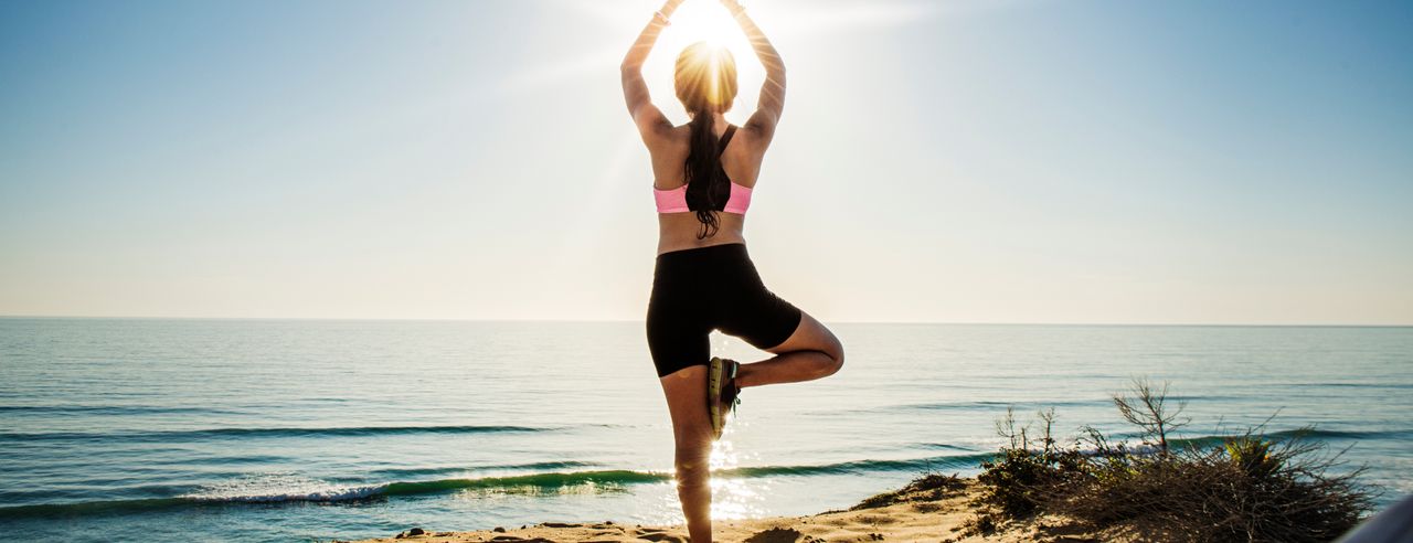 Eine Frau übt ihre Yoga Asanas am Strand von Binz bei Sonnenaufgang