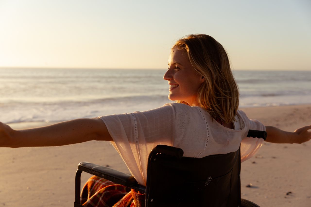 Frau im Rollstuhl am Strand bei Sonnenuntergang