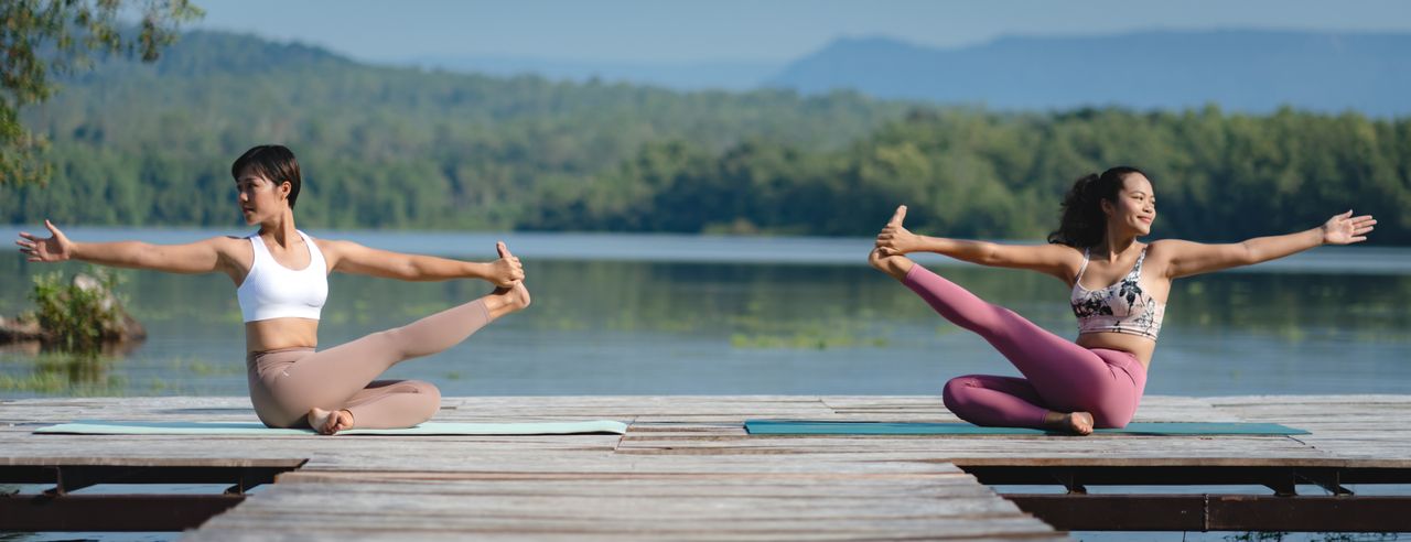 Zwei Frauen praktizieren Yoga an einem See in Mecklenburg-Vorpommern. Sie freuen sich über den Sonnenschein und ihre Yoga Praxis.