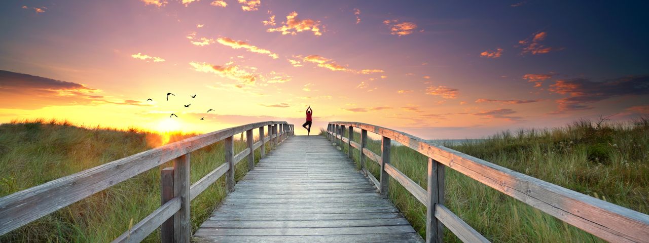 Eine Frau praktiziert Yoga auf Rügen mit dem Blick aufs Meer auf einem Steg.