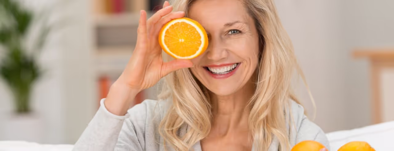Eine Frau hält eine aufgeschnittene Orange vor ihr Auge