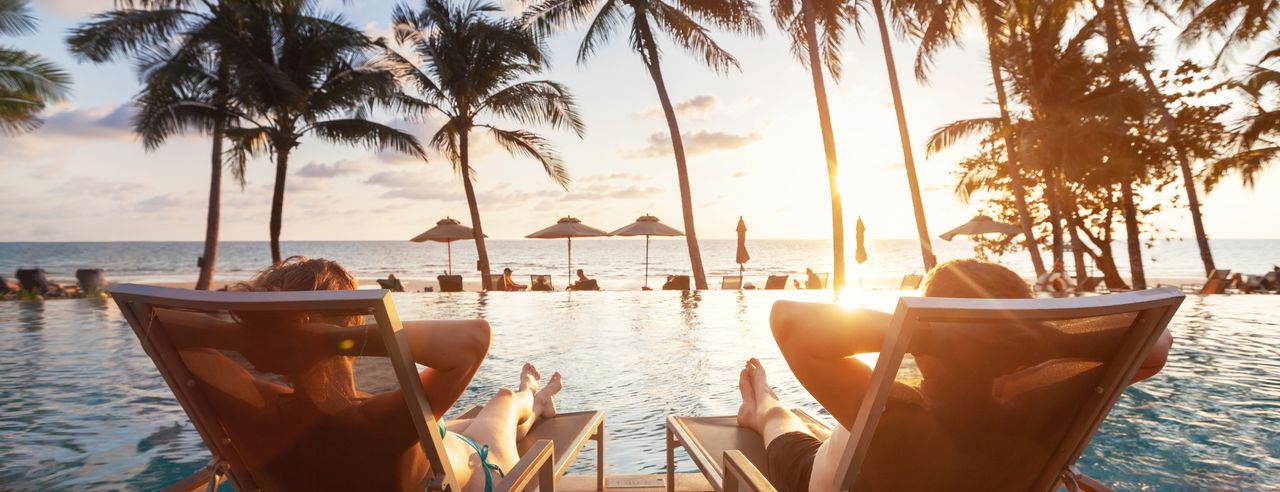 Paar entspannt am Pool unter Palmen bei einem Urlaub mit Wellness Angeboten