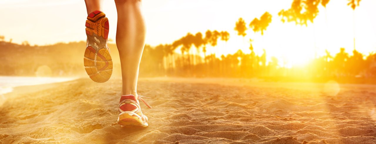 Eine Person läuft in Sportschuhen im Sonnenuntergang am Strand der Sonne entgegen