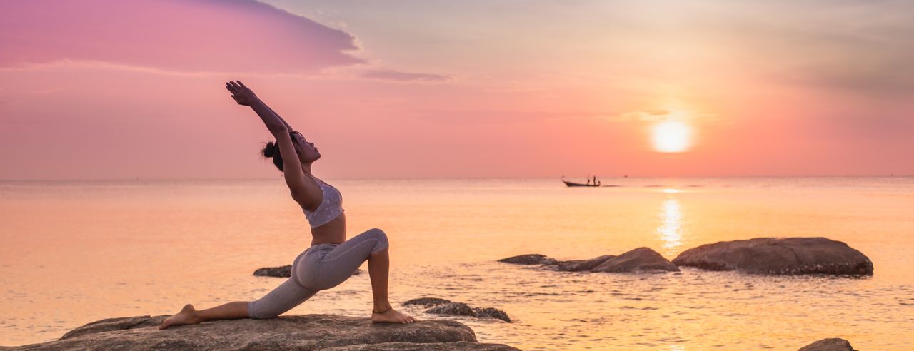 Frau in Yogastellung auf einem Felsen am Meer bei Sonnenuntergang