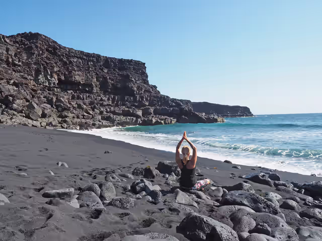 Eine Frau macht Yoga am schwarzen Strand