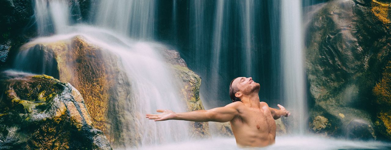 Mann steht unter einem Wasserfall