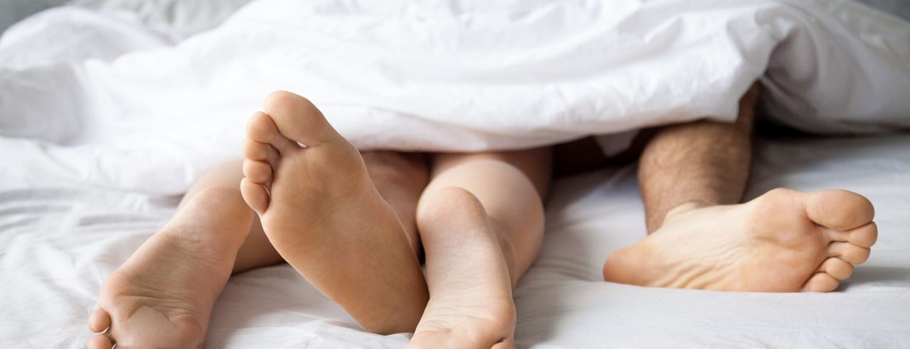 2 Paar Nackte Füße und Beine schauen unter einer Bettdecke hervor