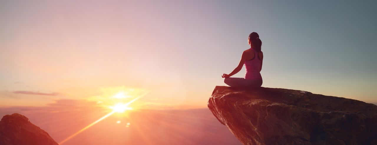 Frau im Lotussitz auf einem freischwebenden Felsen bei Sonnenaufgang