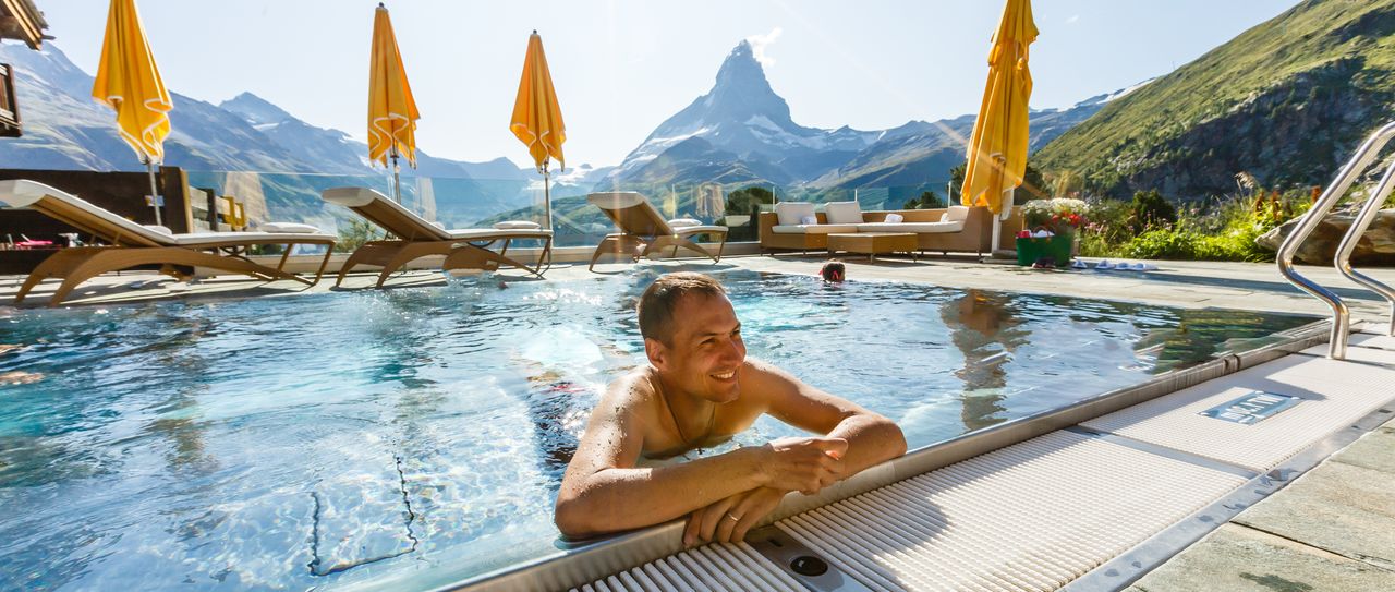 Ein Mann im Außenpool eines Hotels mit Bergblick