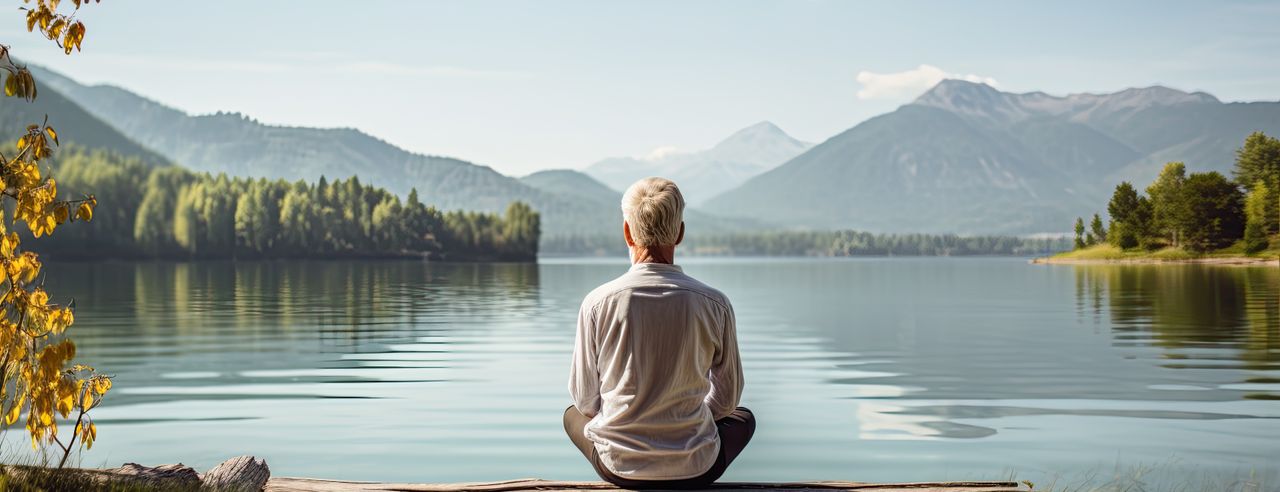 Älterer Mann übt Yoga an einem ruhigen See in einer natürlichen Umgebung