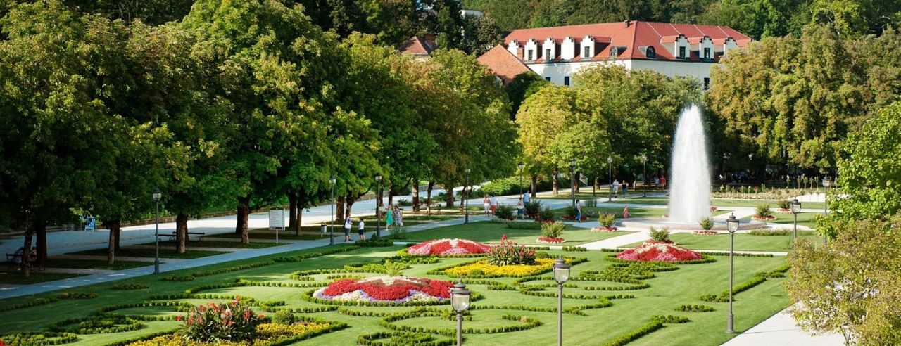 Parkanlage mit bunten Blumenbeeten, Springbrunnen und Spaziergängern im Grünen