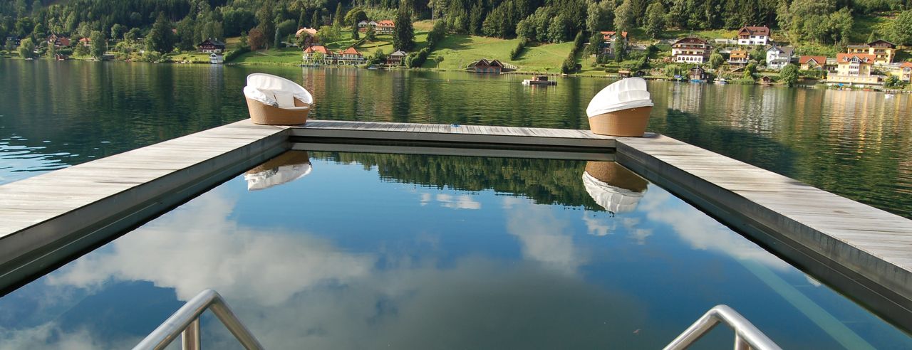 Hotel mit Infinity Pool am See in Bayern, im Hintergrund Berglandschaft