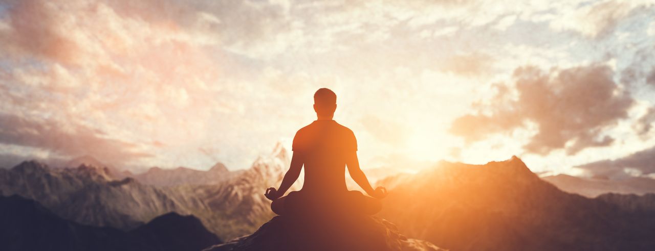 Mann während einer Meditation im Sonnenaufgang in den Bergen