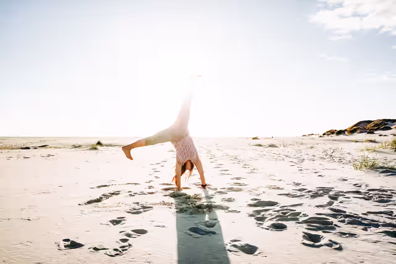 Eine Frau schlägt ein Rad an einem weißen Sandstrand an der Nordsee.