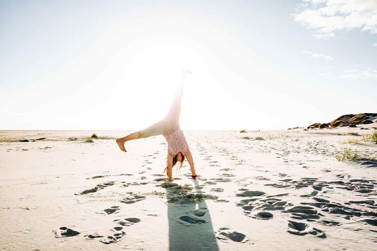Eine Frau schlägt ein Rad an einem weißen Sandstrand an der Nordsee.