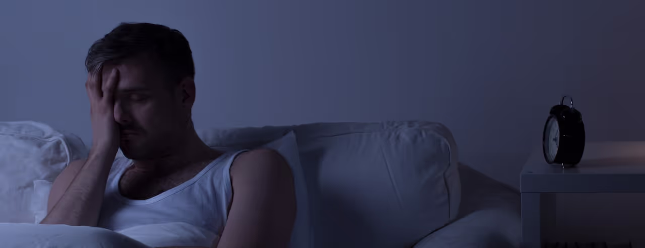 Ein Mann hält sich verzweifelt das Gesicht Nachts, weil er nicht schlafen kann