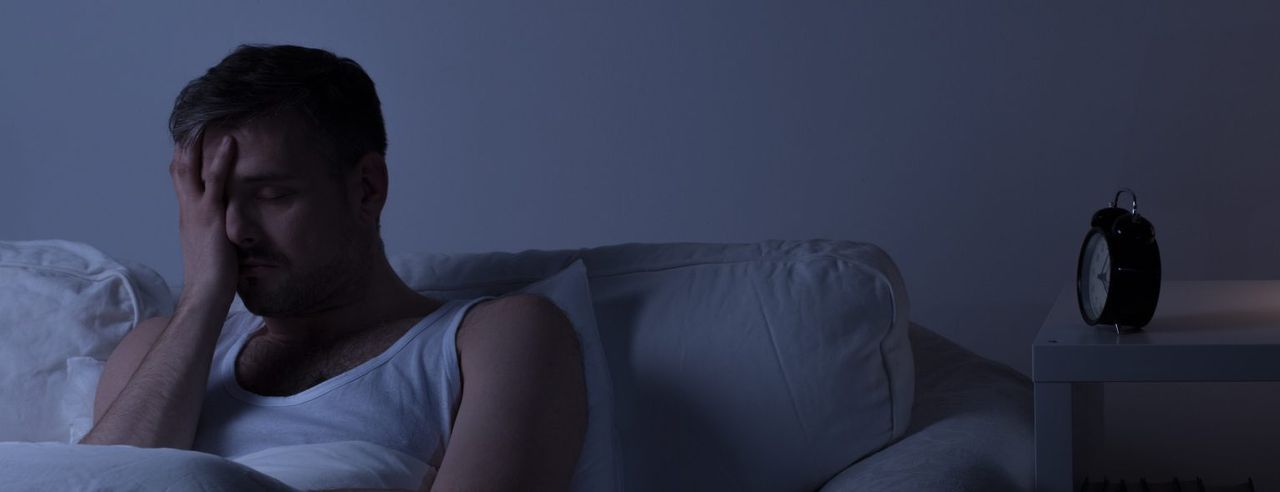 Ein Mann hält sich verzweifelt das Gesicht Nachts, weil er nicht schlafen kann