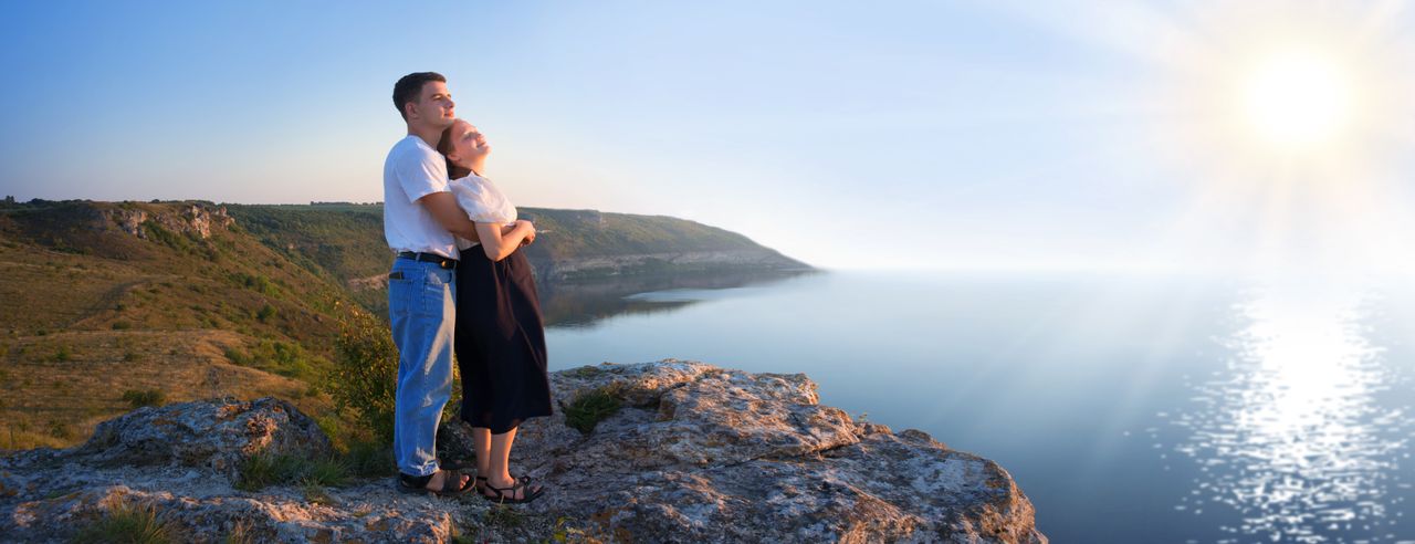 Mann umarmt seine schwangere Partnerin mit Blick aufs Meer