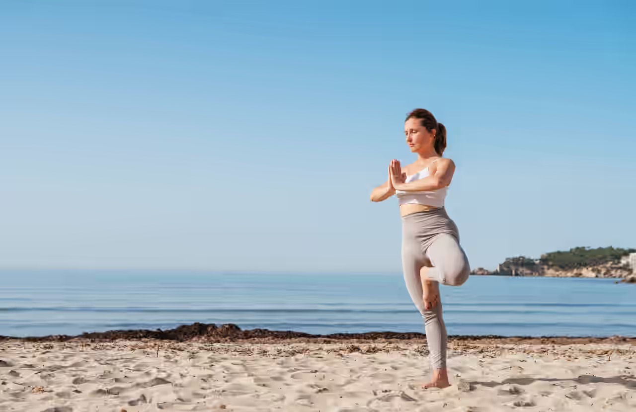 Eine Frau steht in einer Yoga-Pose am Strand.
