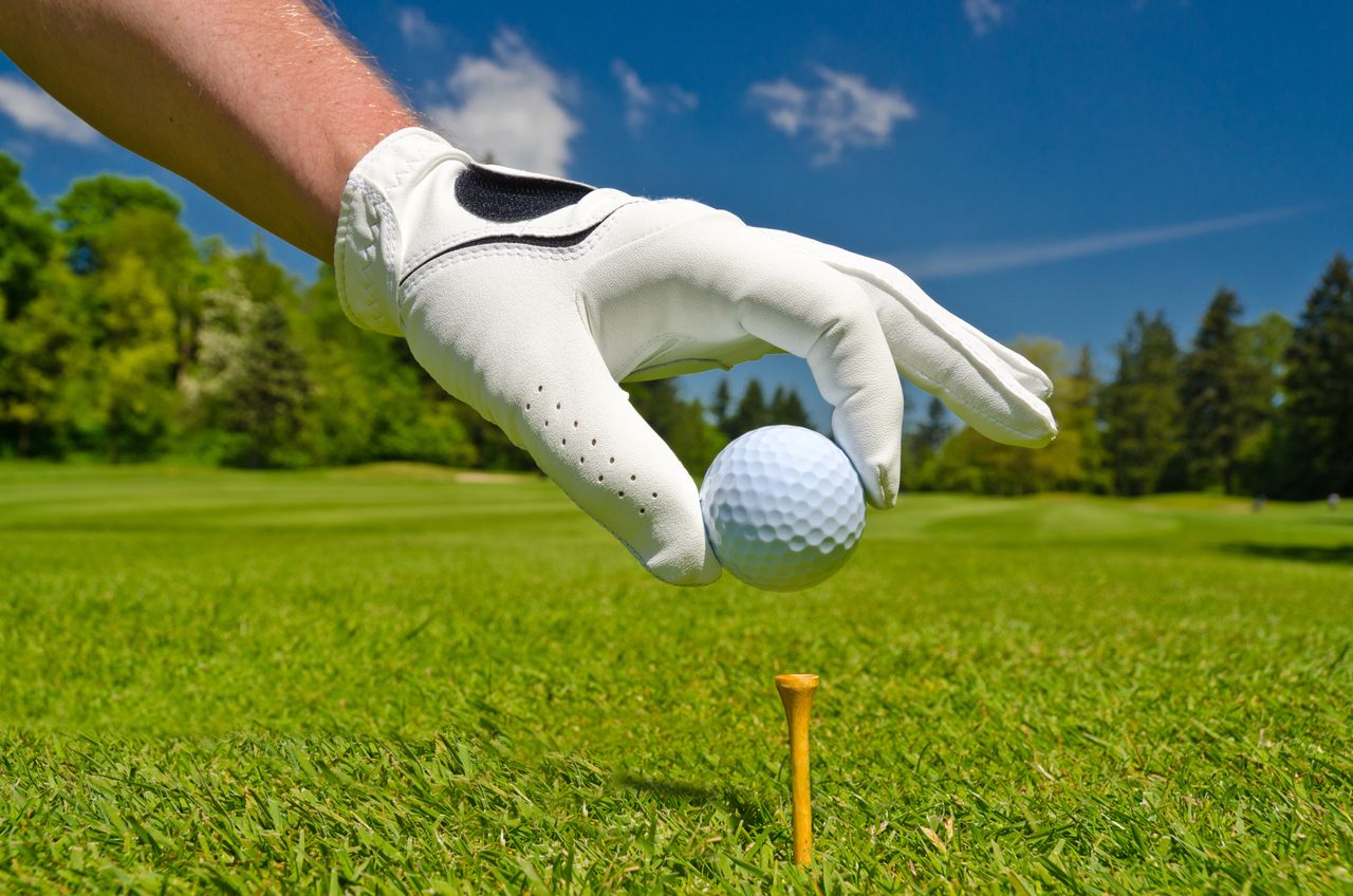 Hand im weißen Golfhandschuh legt Ball auf das Tee