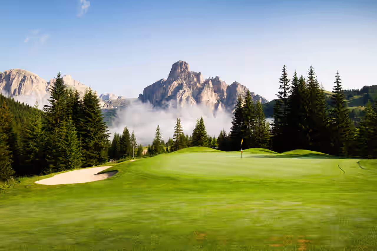 Blick auf einen Golfplatz, umgeben von Bäumen mit Bergen im Hintergrund