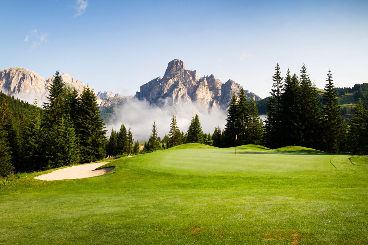Blick auf einen Golfplatz, umgeben von Bäumen mit Bergen im Hintergrund