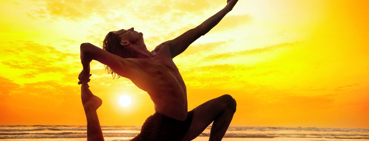 Mann in Yoga Position vor einem Sonnenuntergang am Meer