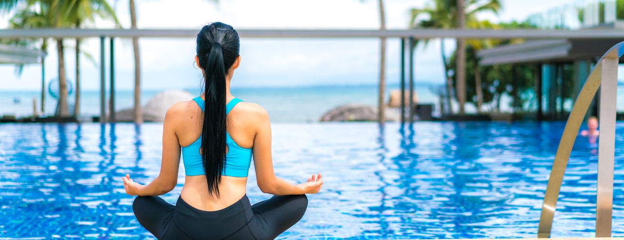 Woman doing yoga by the pool of her yoga and wellness hotel