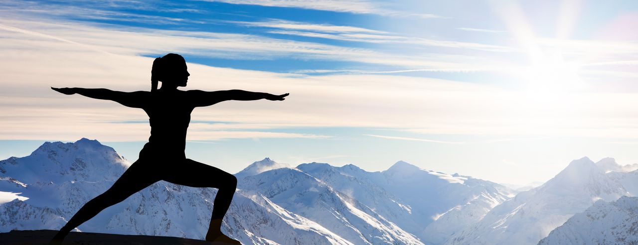 Frau in Yogastellung vor einer beeindruckenden schneebedeckten Bergwelt
