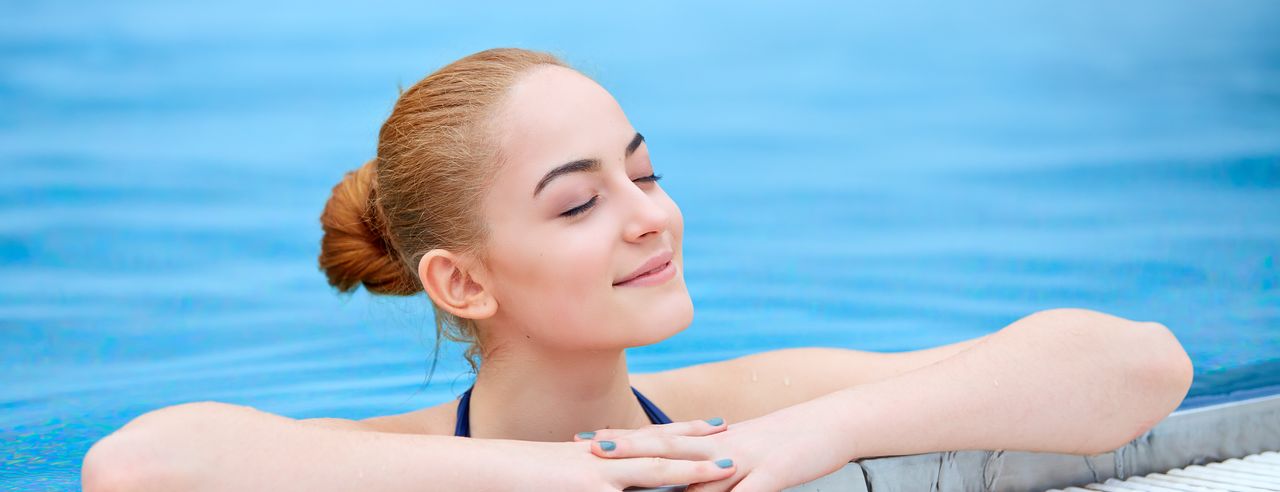 Frau im Pool lehnt sich über den Beckenrand