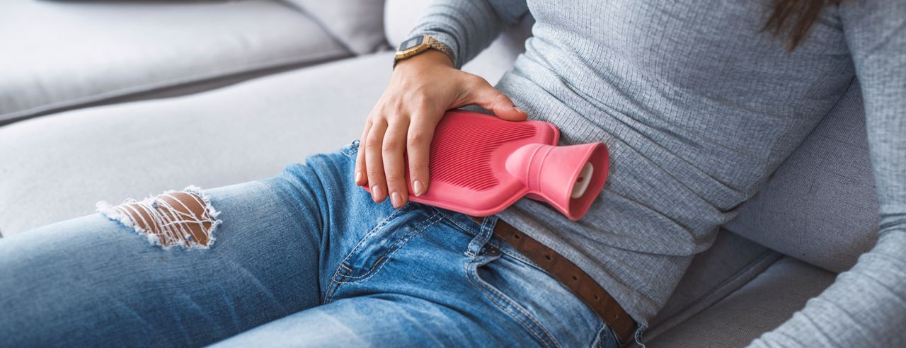 Una mujer sostiene una bolsa de agua caliente sobre su abdomen dolorido