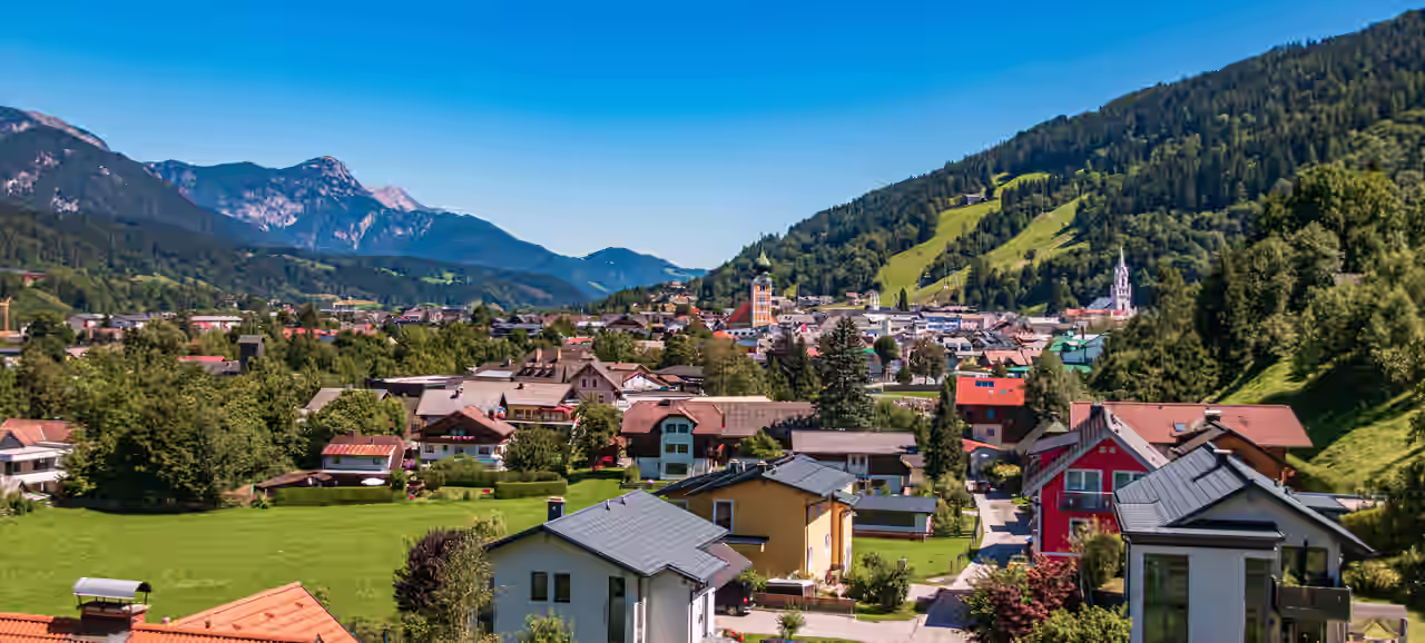 Blick auf Schladming im Sonnenschein zwischen grünen Wiesen und bewaldeten Hügeln