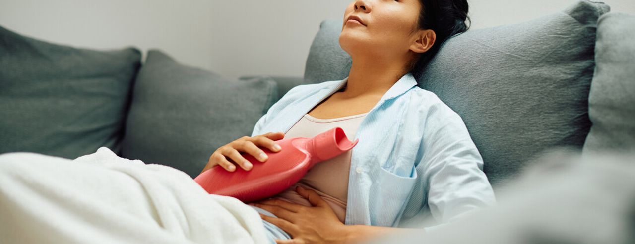 Frau mit Wärmflasche hat Bauchschmerzen