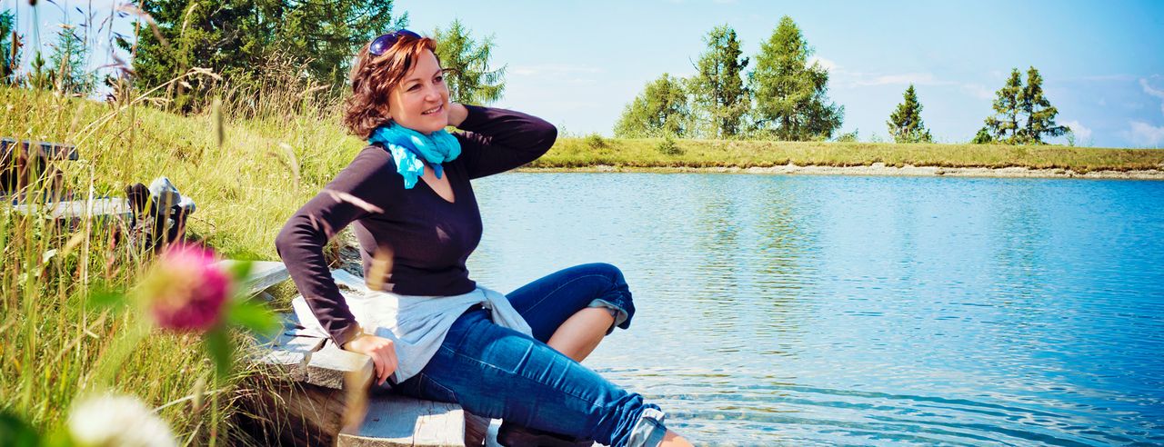 Frau sitzt auf einer Holztreppe am See und hält einen Fuß ins Wasser