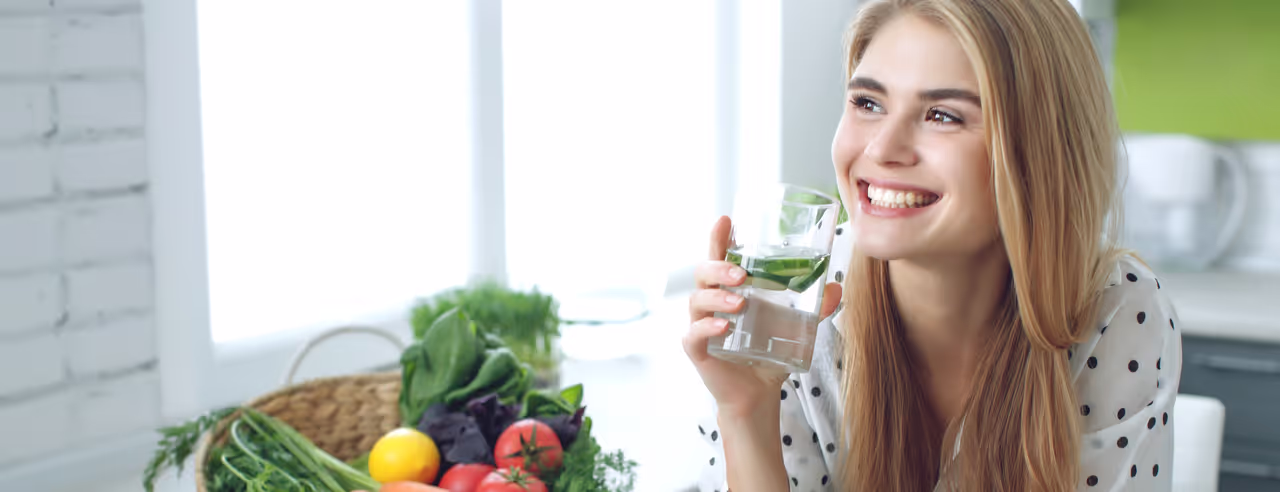 Junge, glückliche Frau isst einen gesunden Salat und sitzt an einem Tisch mit frischen, grünen Zutaten.