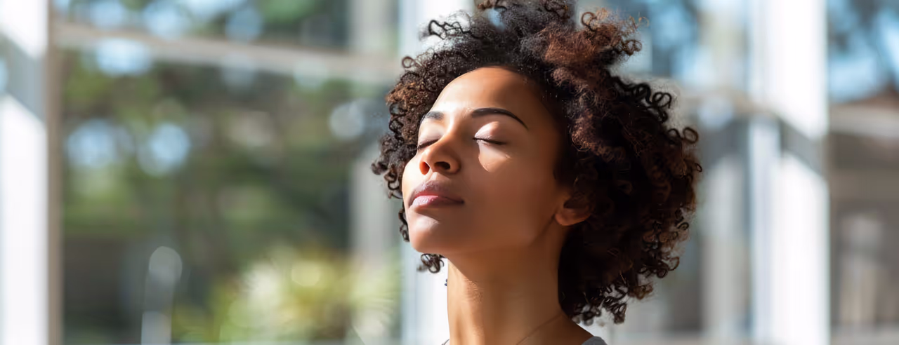 Une femme se tient dans un studio de yoga lumineux, les yeux fermés et la tête penchée vers le haut.