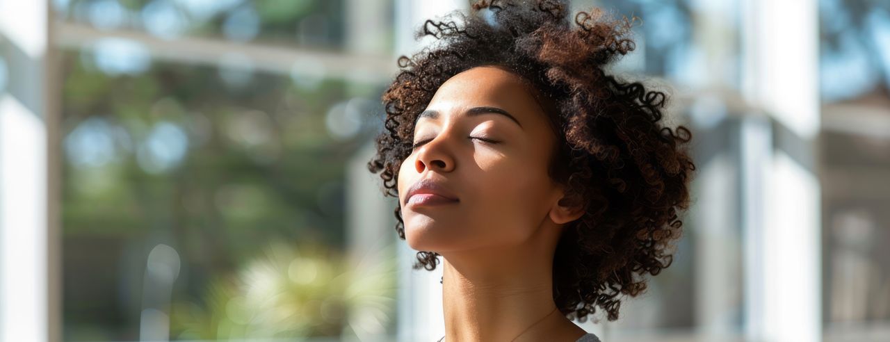 Une femme se tient dans un studio de yoga lumineux, les yeux fermés et la tête penchée vers le haut.