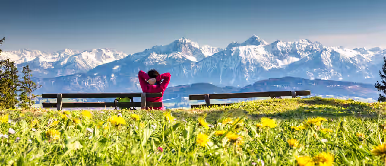 Eine Frau auf einer Bank mit Panoramablick auf die Alpen