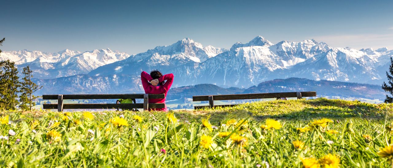 Eine Frau auf einer Bank mit Panoramablick auf die Alpen