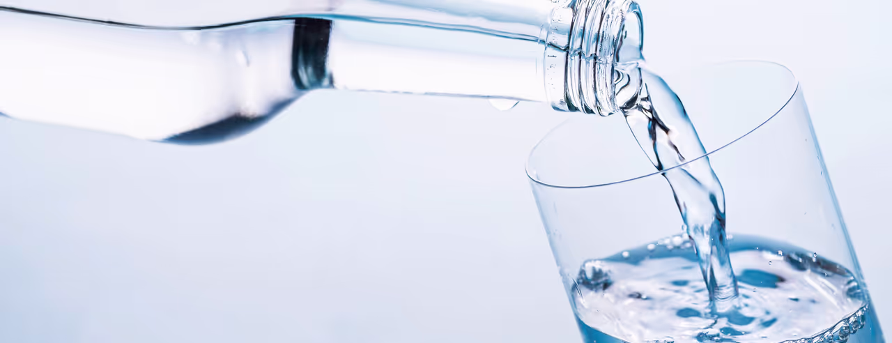 Aus einer Glasflasche fließt Wasser in ein Glas