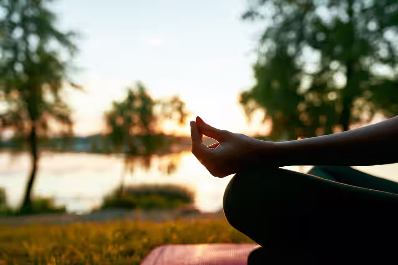 Eine Frau sitzt im Lotussitz an einem Fluss bei Sonnenaufgang in England in ihrem Yoga Urlaub
