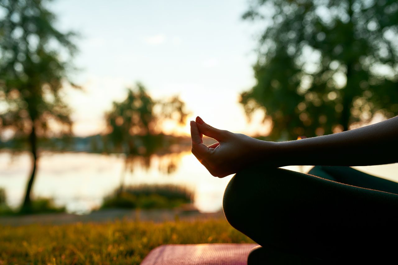 Eine Frau sitzt im Lotussitz an einem Fluss bei Sonnenaufgang in England in ihrem Yoga Urlaub