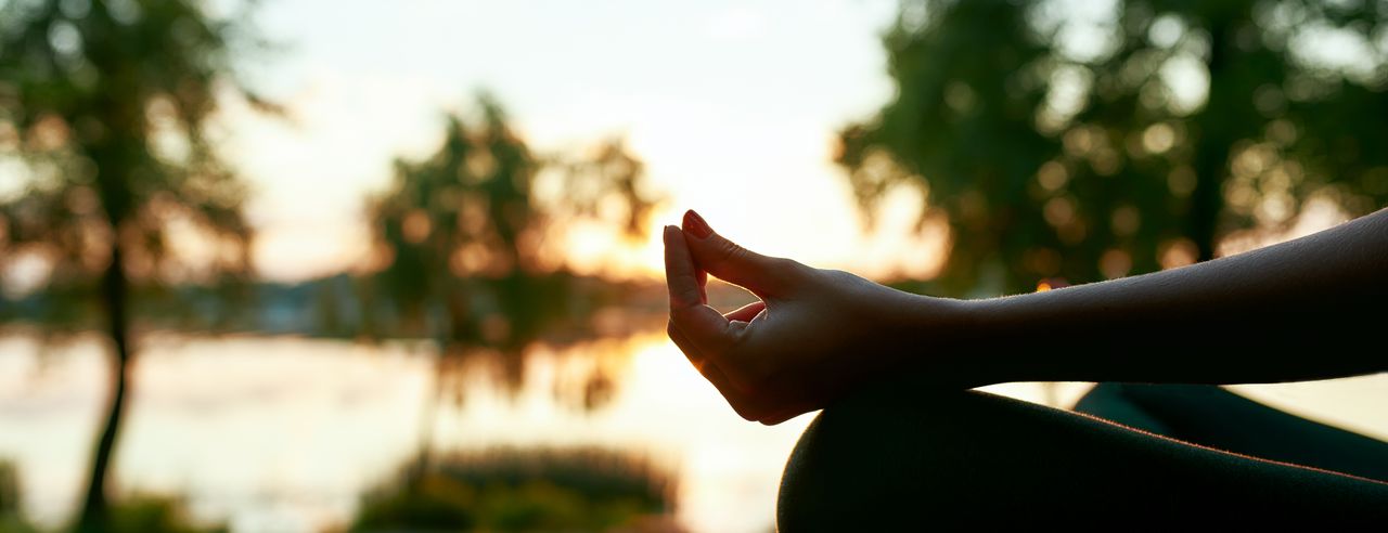 Eine Frau sitzt im Lotussitz an einem Fluss bei Sonnenaufgang in England in ihrem Yoga Urlaub