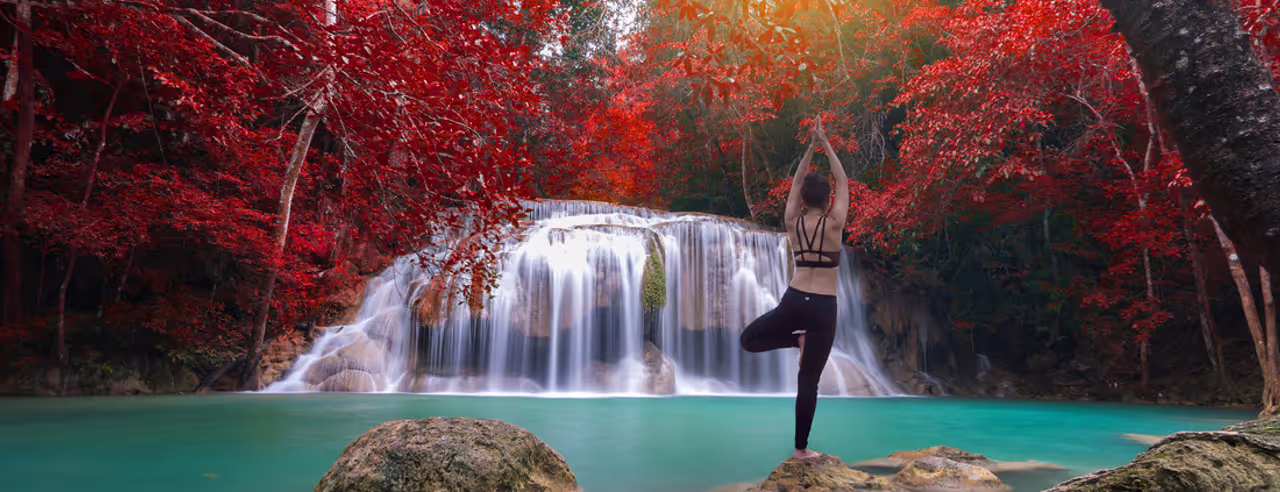 Eine Frau übt Yoga draußen an einem Wasserfall im Herbst