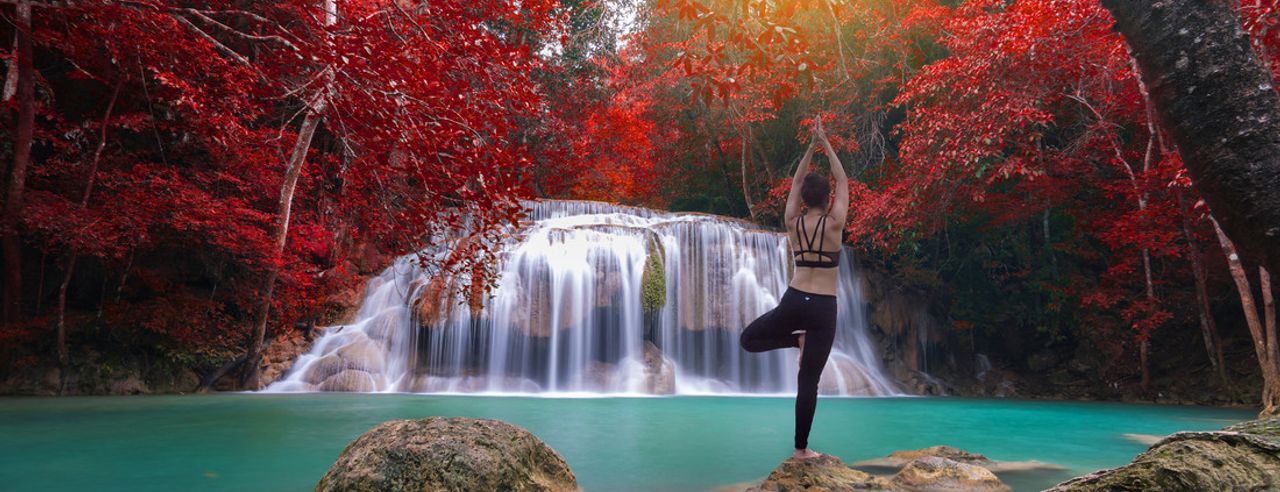 Eine Frau übt Yoga draußen an einem Wasserfall im Herbst