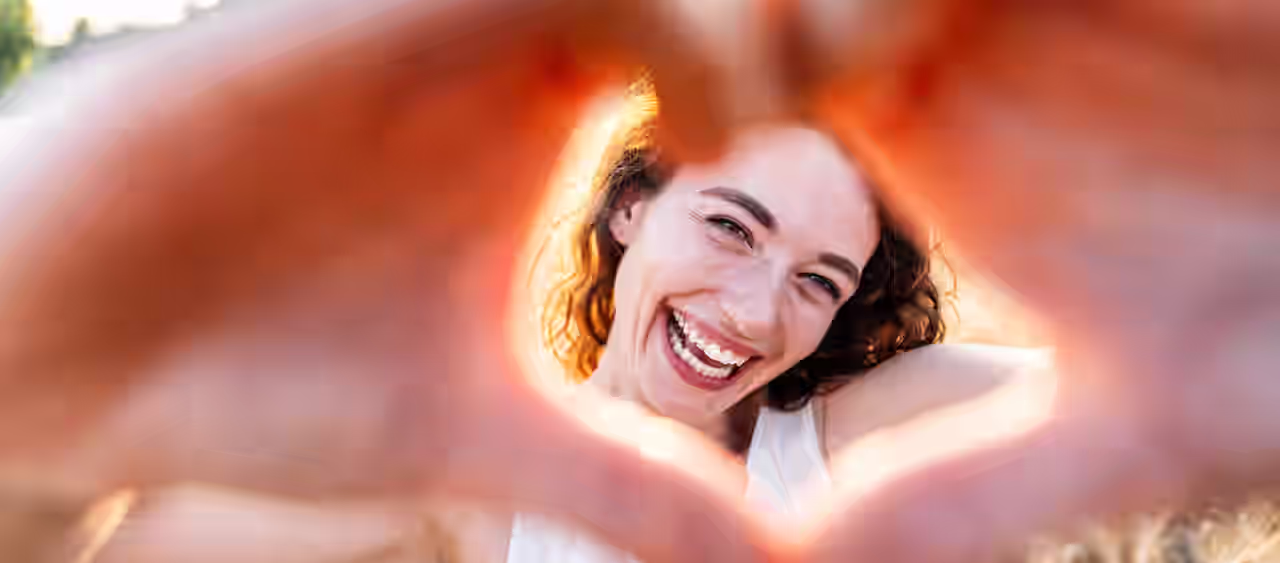 Eine fröhliche Frau rahmt ihr Gesicht mit zu einem Herz geformten Händen ein