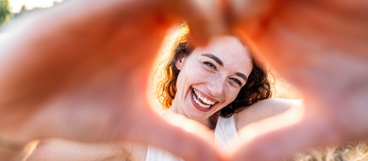 Eine fröhliche Frau rahmt ihr Gesicht mit zu einem Herz geformten Händen ein