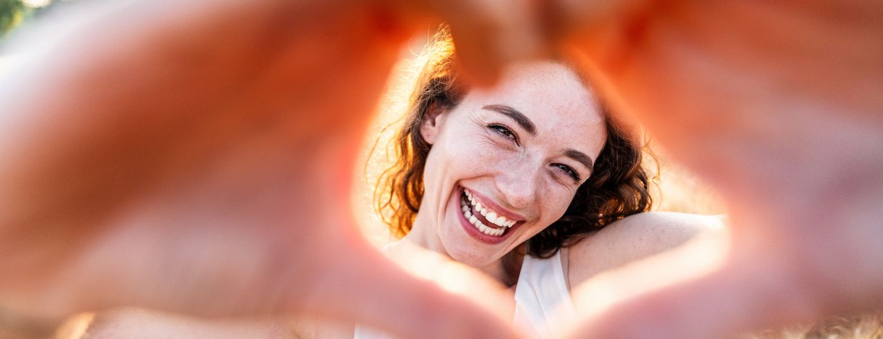 Eine fröhliche Frau rahmt ihr Gesicht mit zu einem Herz geformten Händen ein