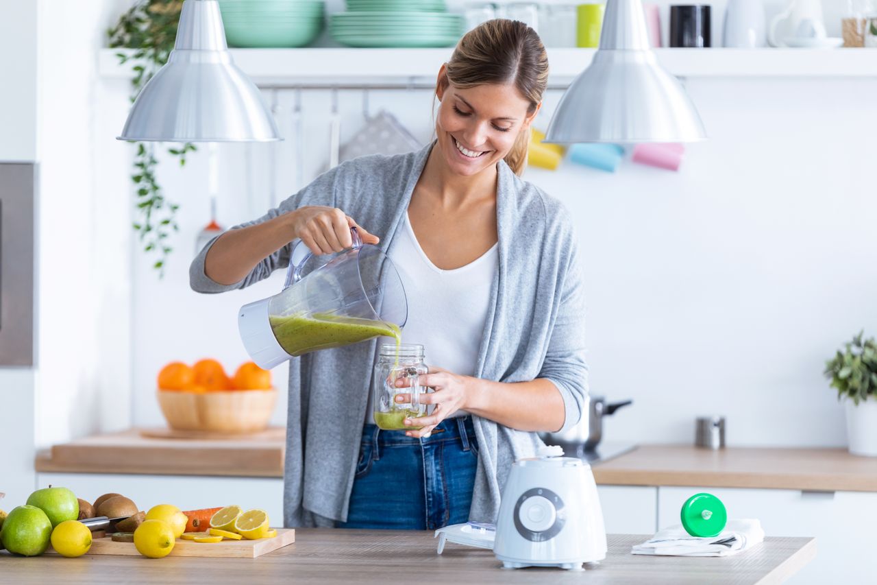 Lächelnde Frau gießt sich einen frischen Smoothie ein