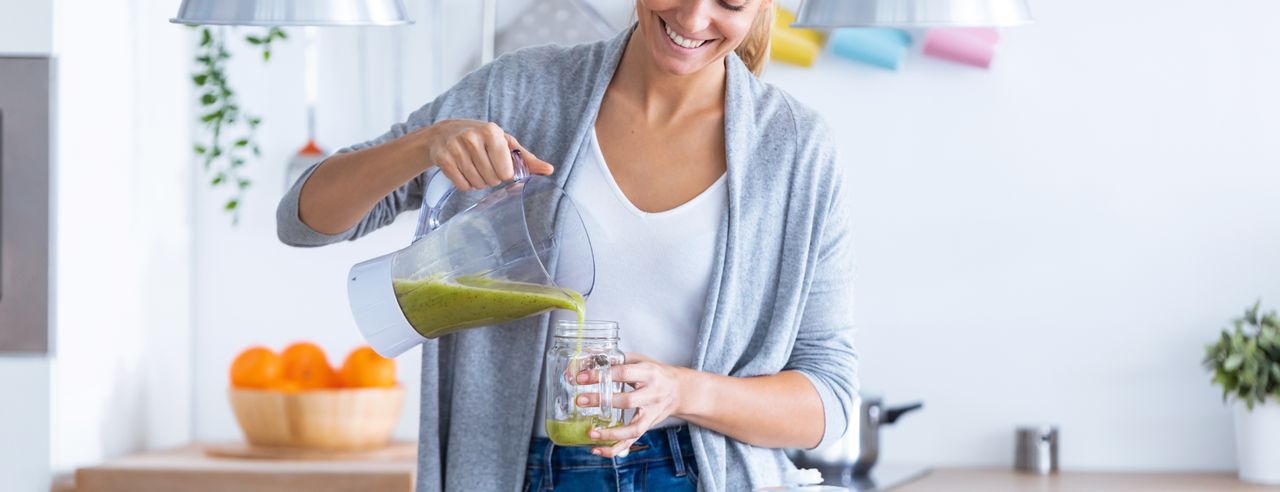 Lächelnde Frau gießt sich einen frischen Smoothie ein